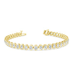 A gold-colored bezel set oval tennis bracelet featuring diamonds.
