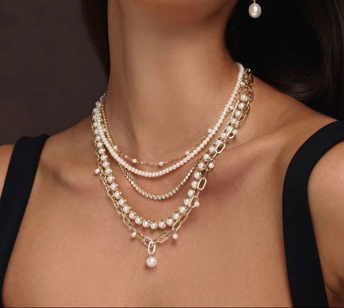Close-up of a woman wearing multiple pearl necklaces and earrings against a dark background