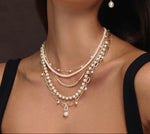 Close-up of a woman wearing multiple pearl necklaces and earrings against a dark background