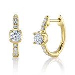 A pair of 14k gold metal huggie earrings with a central diamond and smaller clear stones.
